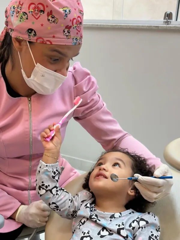 Dentista da WA atendendo uma criança, que segura uma escova de dentes